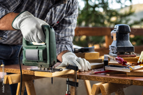 Obraz na plátně Adult carpenter craftsman wears protective leather gloves, with electric saw working on cutting a wooden table