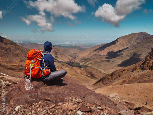 Tourist girl sits on the rock in High Atlas mountains and enjoyis view of the valley near Imlil in Morocco