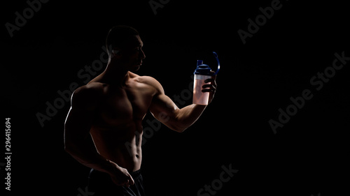 Model sports young man on dark background. Portrait of sporty strong muscle guy with protein drink in shaker. Sexy torso. Bodybuilding nutrition supplements, sport, workout, healthy lifestyle concept.