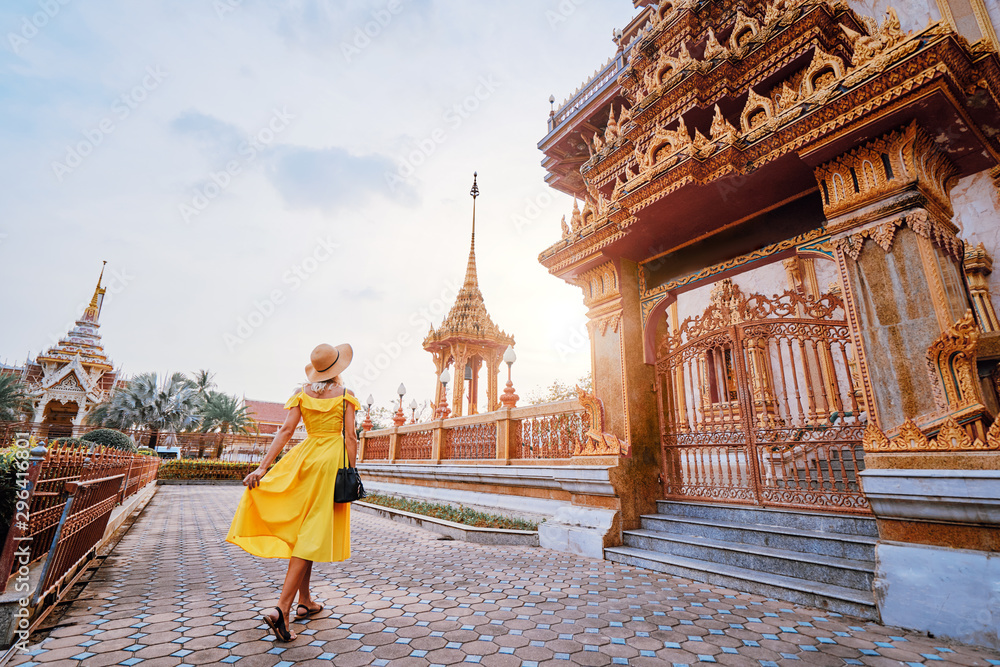 Naklejka premium Podróż przez Azję. Młoda kobieta w kapeluszu i żółtej sukience spaceru w pobliżu świątyni buddyjskiej Chalong na wyspie Phuket w Tajlandii.