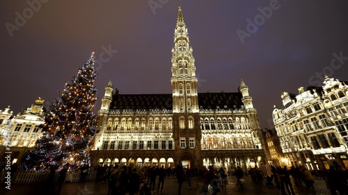 Christmas tree and city hall of Brussels by night, people walk in Grand Place