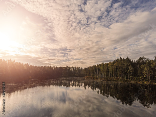 Sunrise over a small lake in a forest, Sun flare, calm atmosphere, Cloudy sky, Reflection in the water.
