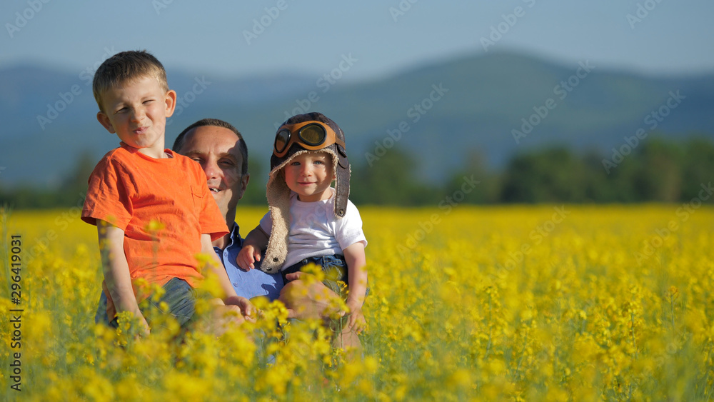 Father with two sons appearing from blossom rape field, have fun in nature