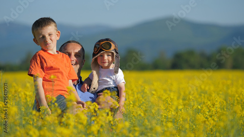 Father with two sons appearing from blossom rape field, have fun in nature