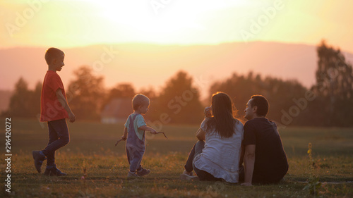 Parents sitting on field  baby child and elder brother come to mother and father