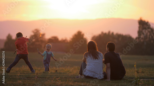 Children playing in nature, parents relax and look to baby child and brother