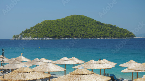 Beach straw umbrellas, turquoise sea and green island, perfect summer holiday