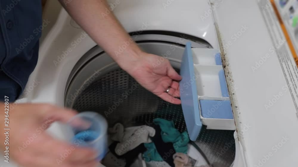 Hand pouring laundry detergent into washing machine dispenser Hand pouring laundry detergent into washing machine dispenser