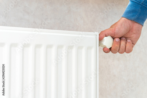Hand adjusting the knob of heating radiator at home a cold season.