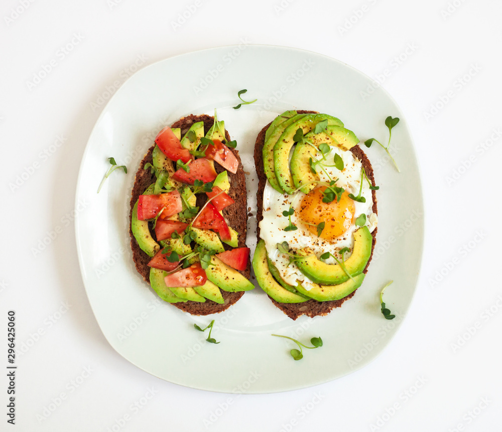 Two toasts of dark bread with avocado slices, chopped tomatoes, fried egg and microgreen. Breakfast concept. Two toasts of dark bread with avocado slices, chopped tomatoes, fried egg and microgreen. Breakfast concept.