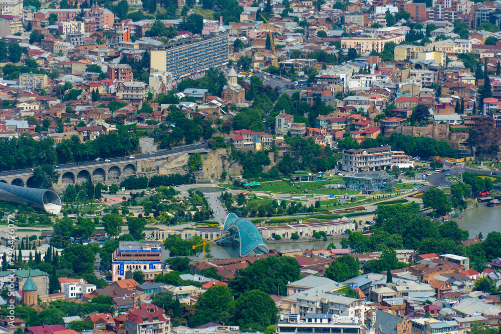 TBILISI, GEORGIA, JUNE 3, 2019: Aerial view from the Narikala fortress on the Tbilisi city, the capital of Georgia, full of small tiled roof houses, green trees, bridges over the Kura river