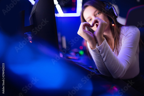 Streamer beautiful girl shows heart sign with hands professional gamer playing online games computer, neon color