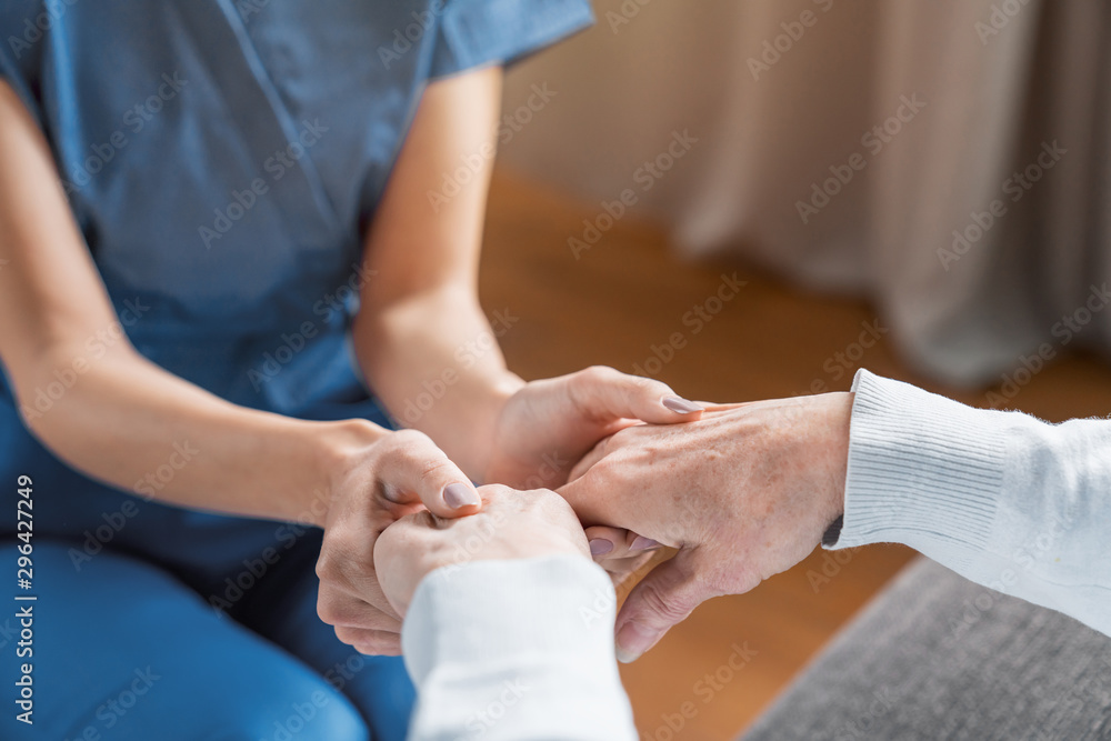 Assisting senior people. Close up of female caregiver holding elderly woman's hands indoors - obrazy, fototapety, plakaty 