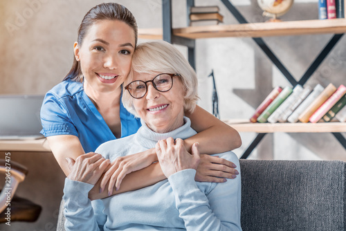Portrait of female caretaker hugging happy elderly woman indoors