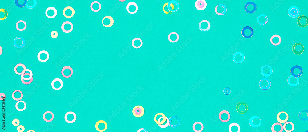 Colorful holographic foil confetti banner background. Pastel colored pink, blue and yellow circles sparse on trendy mint green colored paper. Simple holiday concept. Top view, flat lay, copy space.