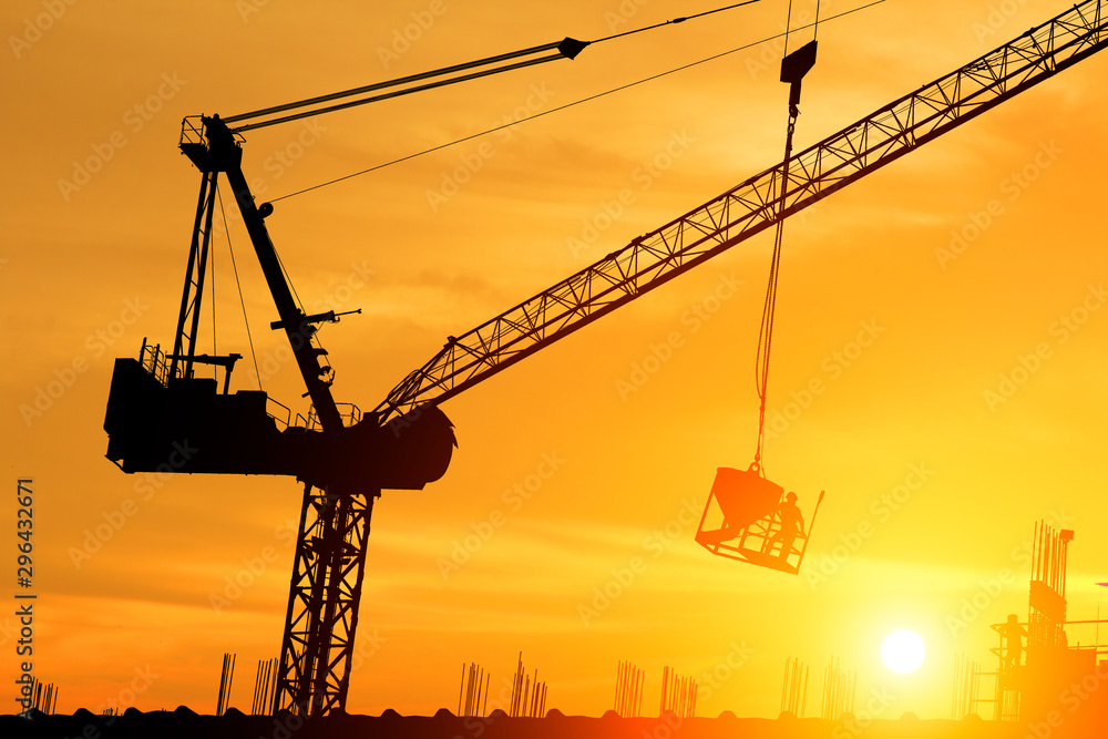 silhouette workers working on cranes on construction sites at sunset.