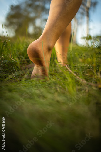 Barefoot young woman in green meadow; Harmony with nature - concept of vacation, summer leisure, naturism, relax