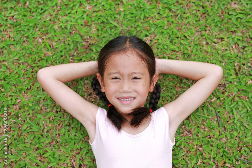 Smiling little Asian child girl with two ponytail hair lying on green grass in the garden. Smiling little Asian child girl with two ponytail hair lying on green grass in the garden.