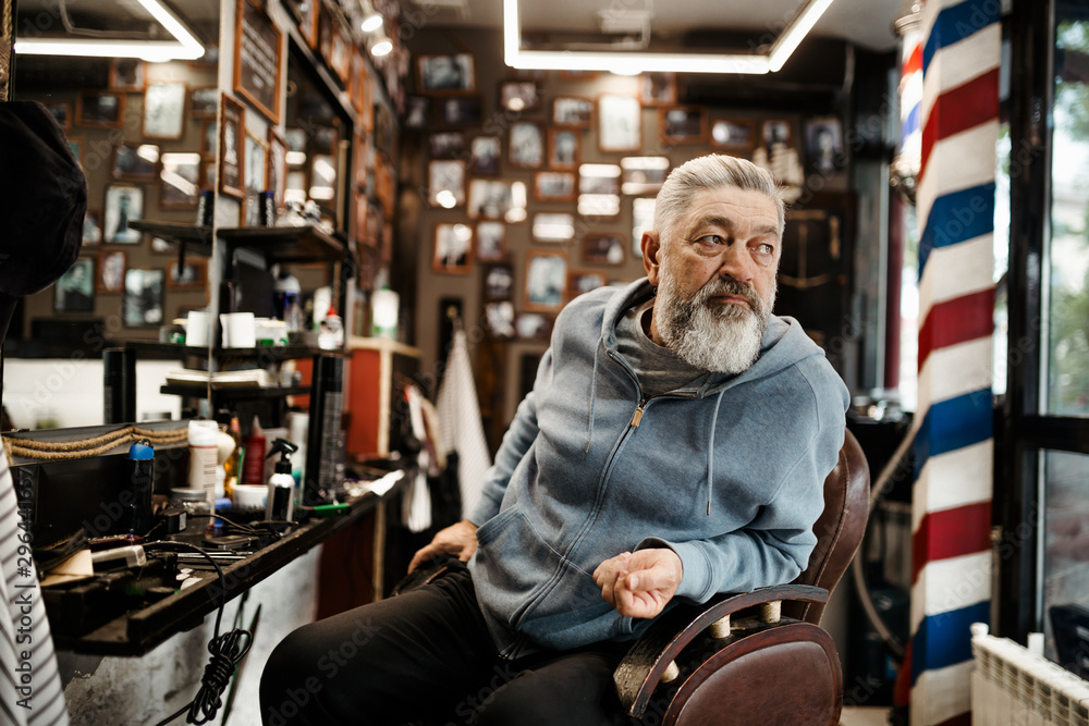 A white haired bearded hipster man sits in a barbershop and waits for his turn to get a haircut A white haired bearded hipster man sits in a barbershop and waits for his turn to get a haircut