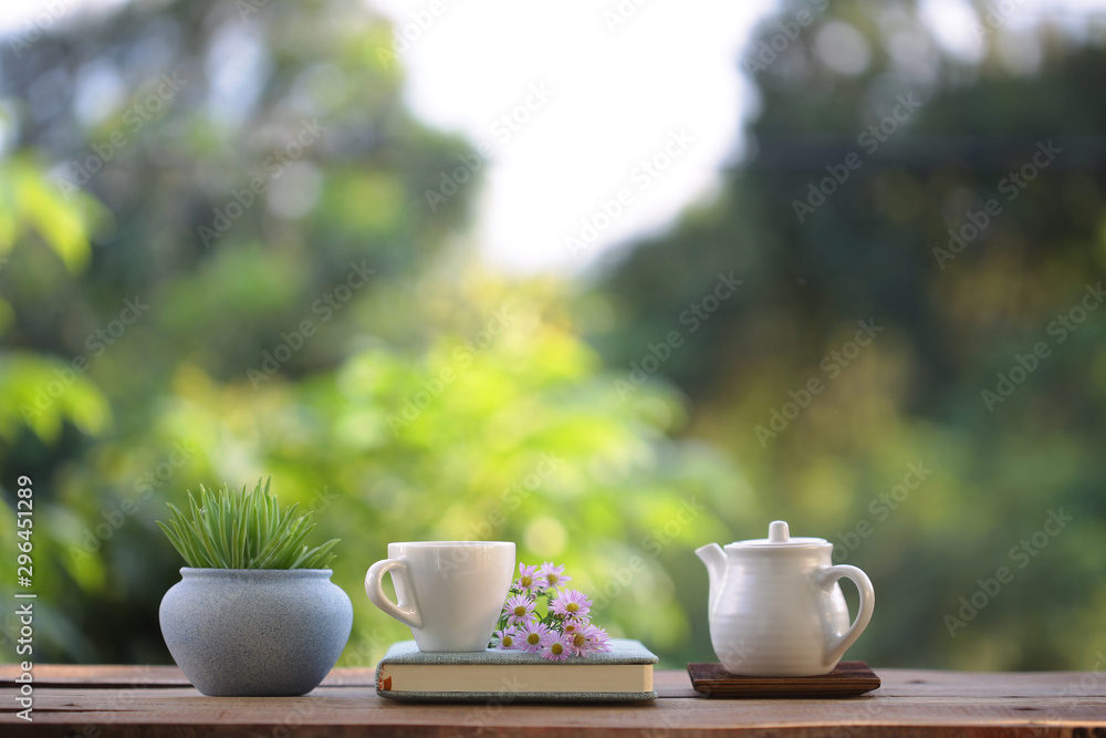 white cup with teapot and small plant with purple daisy flower and book on wooden table white cup with teapot and small plant with purple daisy flower and book on wooden table