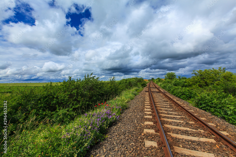 Fototapeta premium Old railroad in remoter rural area in Europe on a summer day, under a sky covered with storm clouds