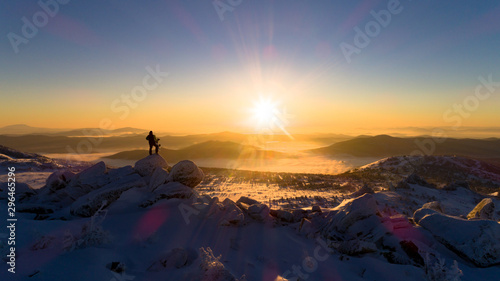 snowboarder on top of mountain in Golden rays of dawn sun. the Freerider stands on the big rocks of a mountain peak above the clouds. Panorama sunset view. Epic free ride scene. Aerial view