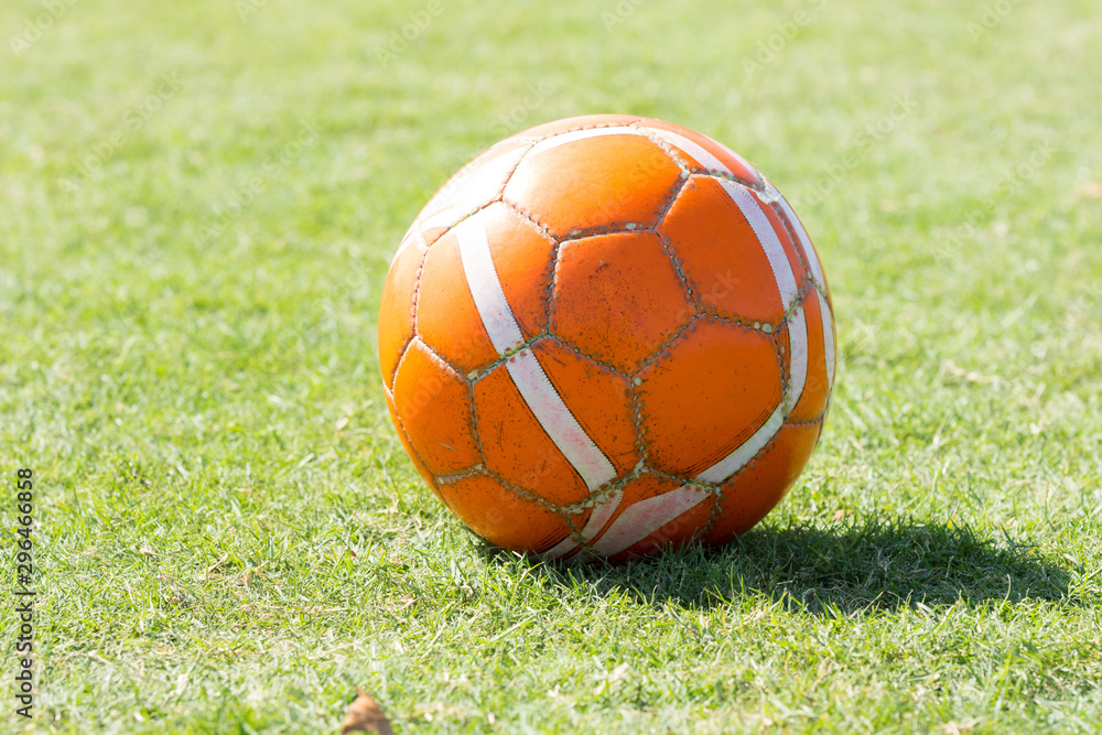 An old rugged used orange soccer ball or football on the ground of grass. An old rugged used orange soccer ball or football on the ground of grass.