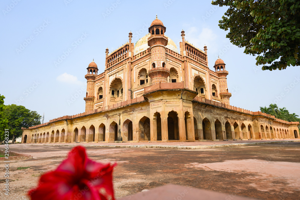 (Selective focus) Stunning view of the Safdarjung Tomb in the background and blurred red Hibiscus flowers in the foreground. New Delhi, India.