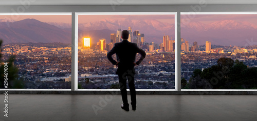 Businessman looking at the buildings of downtown Los Angeles from an office window.  The man looks like a politician like a mayor, or an architect or a real estate developer working in LA.