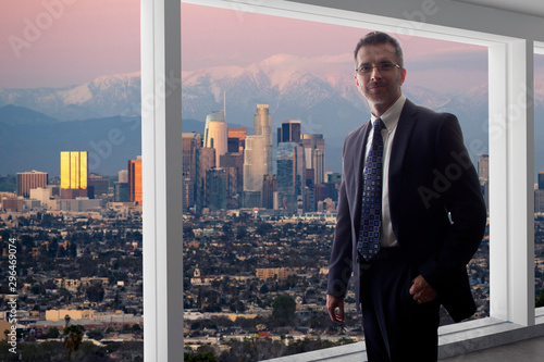 Businessman looking at the buildings of downtown Los Angeles from an office window.  The man looks like a politician like a mayor, or an architect or a real estate developer working in LA.