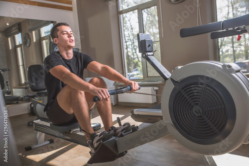 The athlete is engaged in the gym, the Young man works on the rowing simulator