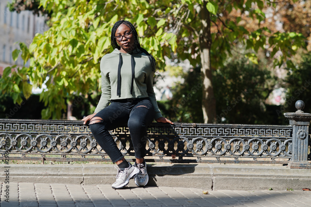 City portrait of positive young dark skinned female wearing green hoody and eyeglasses. City portrait of positive young dark skinned female wearing green hoody and eyeglasses.