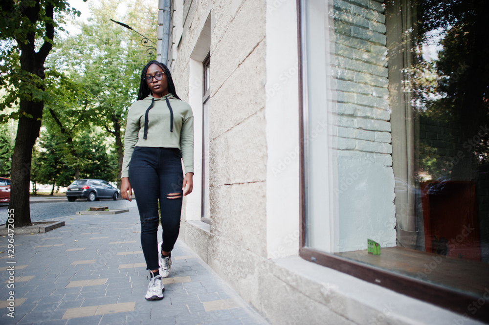 City portrait of positive young dark skinned female wearing green hoody and eyeglasses.