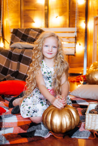 Cute girl of school age with blond long hair in dress an autumn studio with yellow leaves, plaids, pumpkins and apples