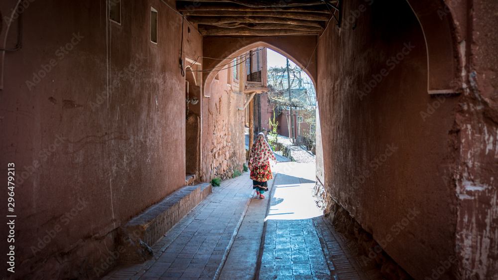 Unidentified woman with traditional Persian clothes walking down a narrow road in Abyahen, Iran