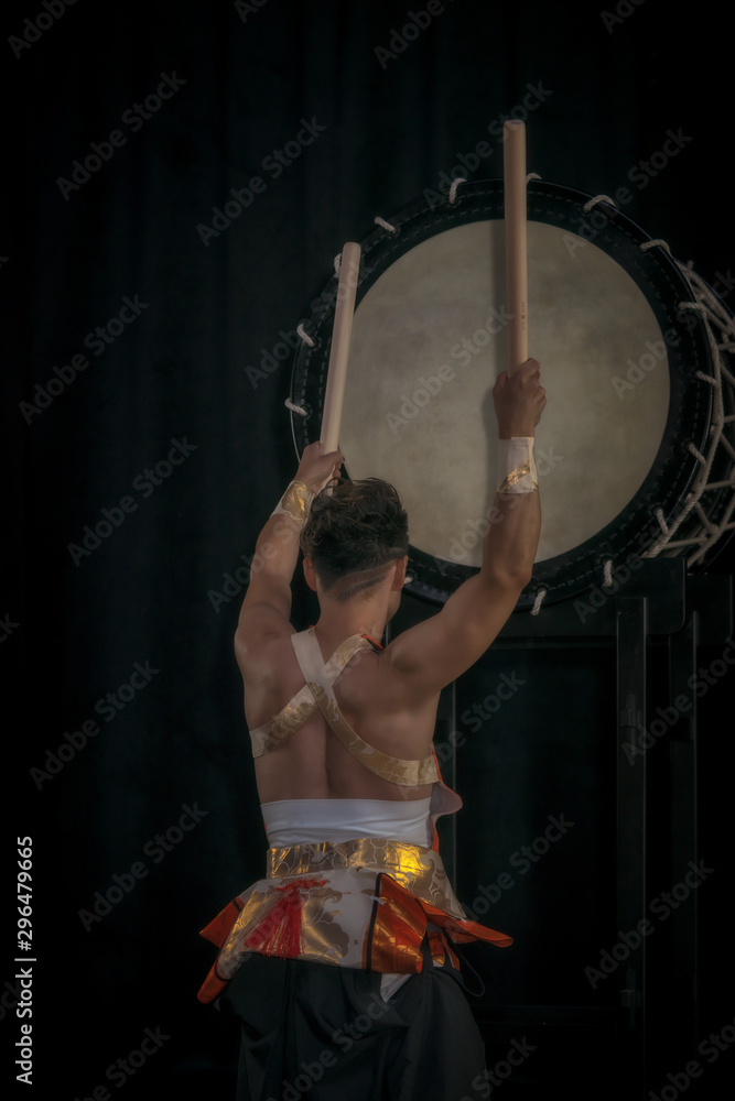 Obraz na plátně Taiko drummer hits the big drum on stage on a black background, back view