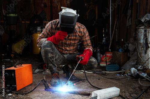 A male welder in a welding mask works with an arc electrode in his garage. Welding, construction, metal work.