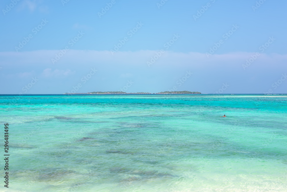 Wide angle picture of the Island on the horizon with bungalows on top of turquoise water in a island located close to Maafushi in Maldives. Picturesque seascape with blue sky.