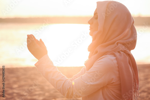 Beautiful Muslim woman praying outdoors at sunset