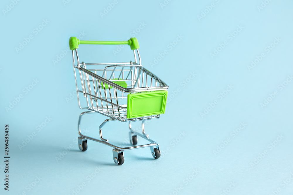Empty small shopping cart on color background