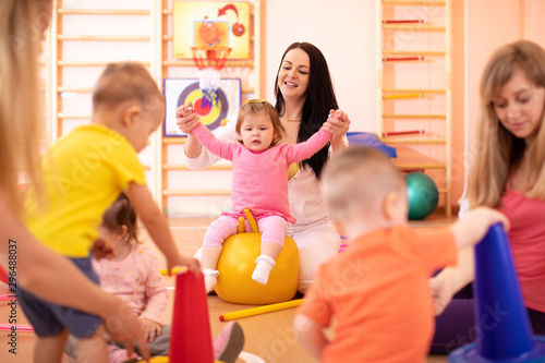 Yoga for baby. Child-friendly fitness for women with kids. Mothers with happy toddlers doing exercises with sportive accessories in gym. Lifestyle concept of parent activity with children.