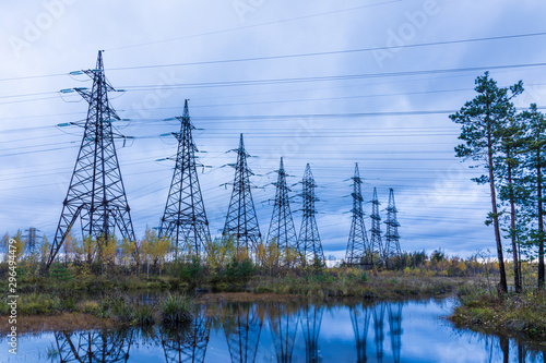 Towers of electric main with the wires in the autumn countryside swamp on the background of blue sky with clouds and the forest 