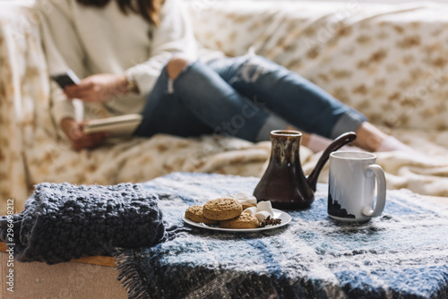 Woman with smartphone on sofa near table with drink and cookies photo