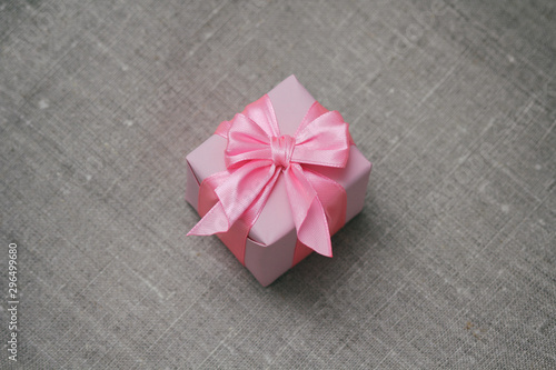 Single square gift box wrapped in pink paper and tie silk ribbon. Cloth decorative background.  © exienator