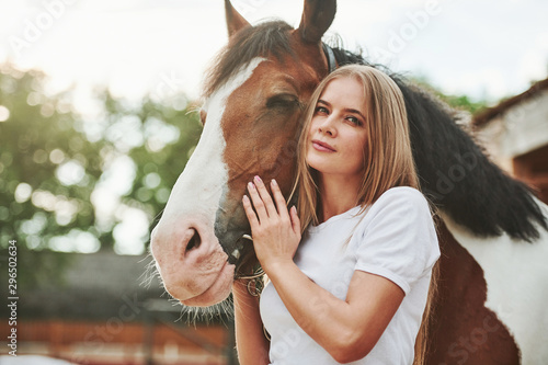 Attractive girl looks straight into the camera. Happy woman with her horse on the ranch at daytime