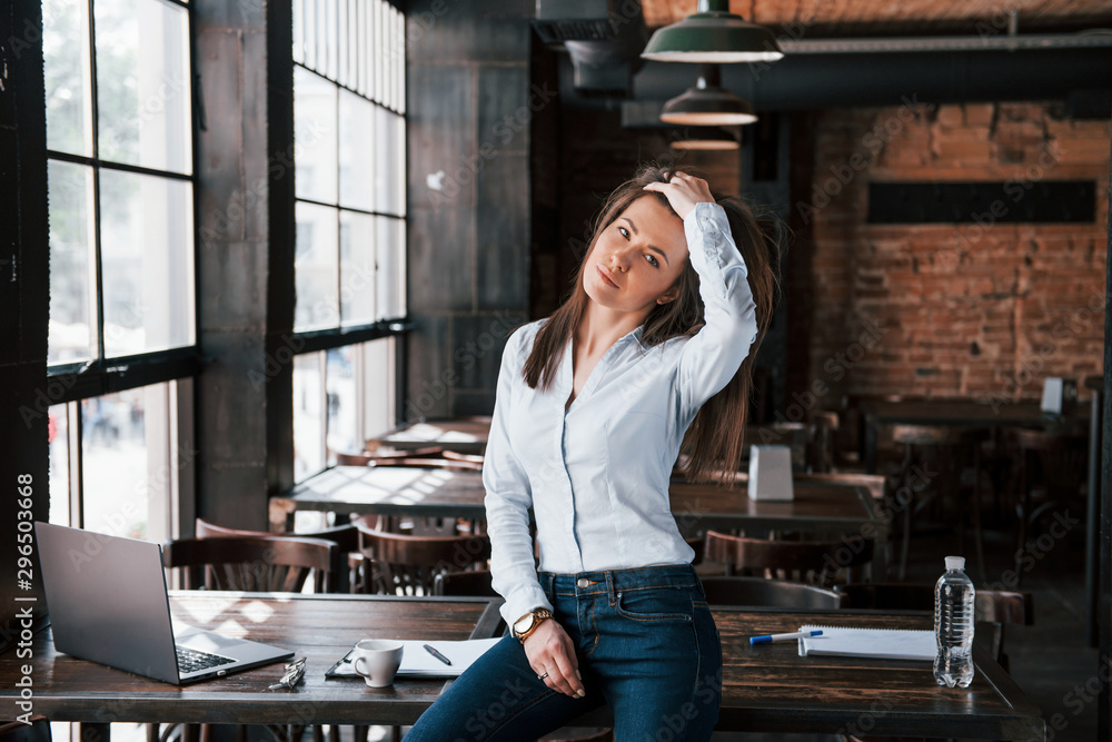 Fototapeta premium Sitting and touching the hair. Businesswoman in official clothes is indoors in cafe at daytime