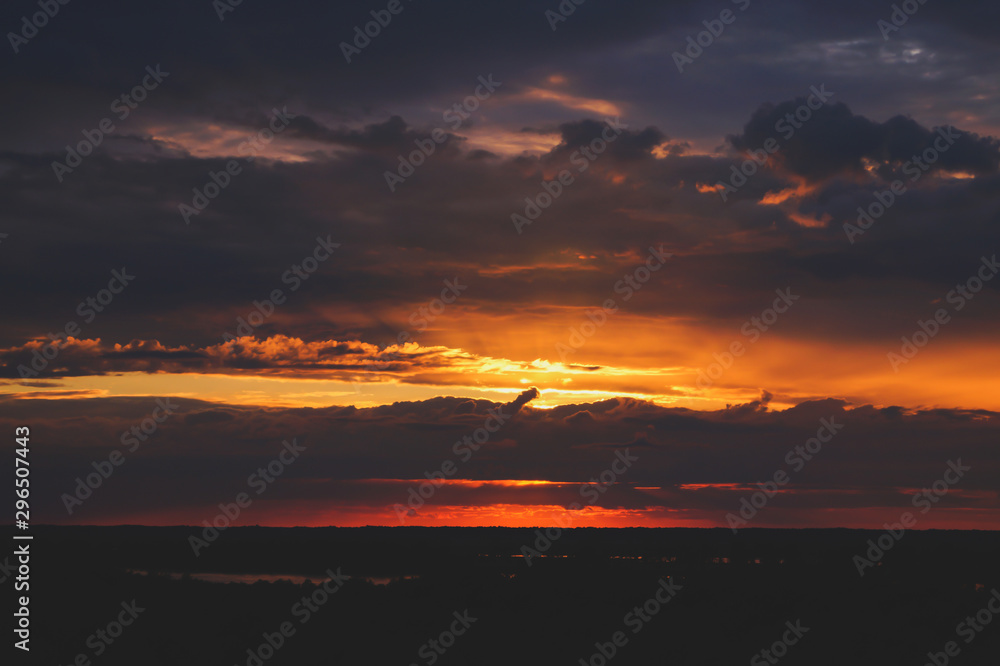 Special sunset over the river and forest. The warm colors of the sun. Bright blue unusual sky. Black silhouette of the forest.