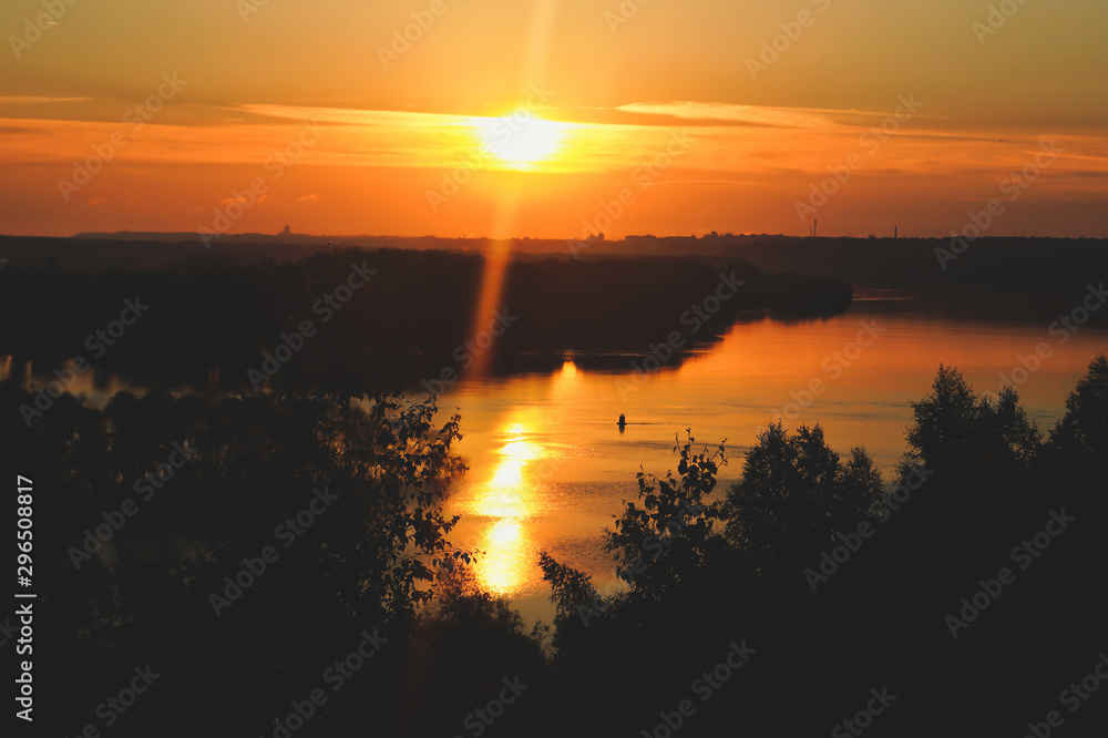 in the rays of the sun, light rises above the horizon and colors the sky, river, forest in orange hues. ripple sun track