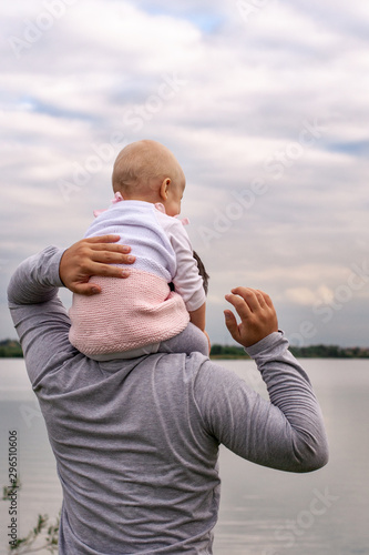 A child on his father’s neck. Walk near the water. Baby and dad against the sky.