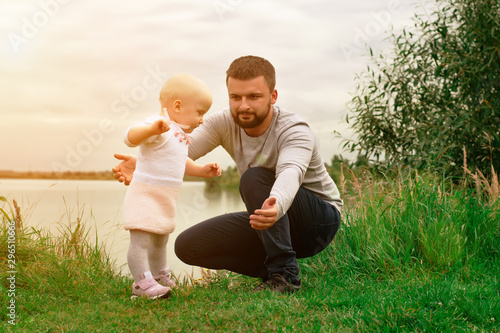 Dad teaches daughter to walk, park, nature. Walk on the grass. Father and daughter. First steps.